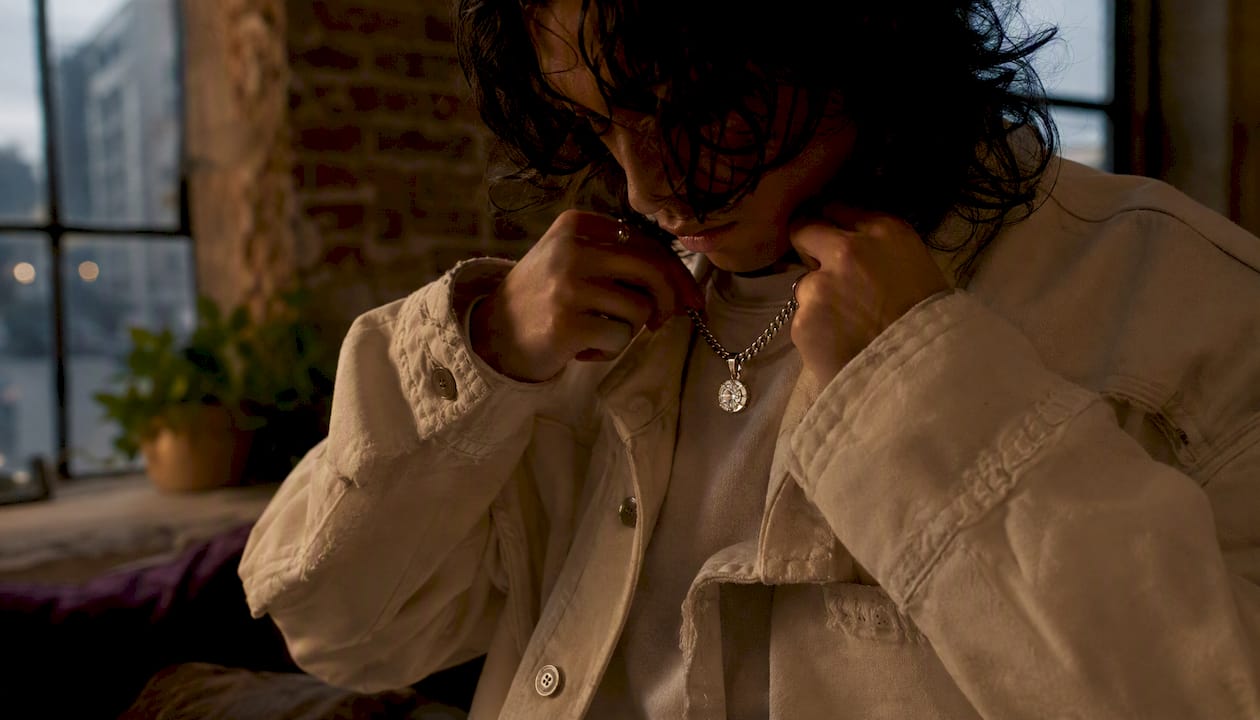 Hands layering ethical gemstone pendant with streetwear