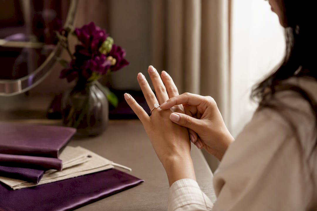 Hand placing moissanite ring on finger near vanity