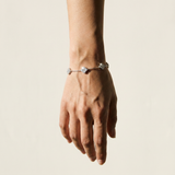 A delicate silver-toned chain bracelet with three small round clear gemstone charms, shown worn on a person's wrist against a plain light beige background.